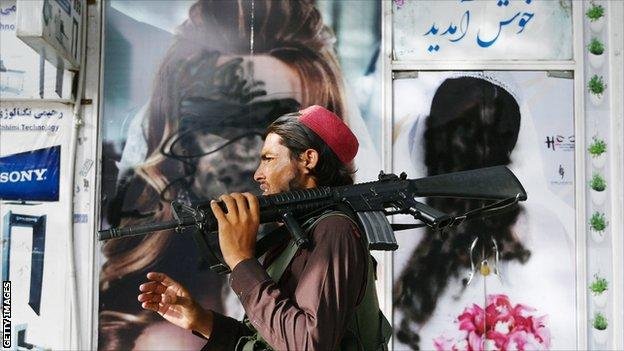 A Taliban fighter walks past a beauty salon with images of women defaced using spray paint in Shar-e-Naw in Kabul on August 18, 2021