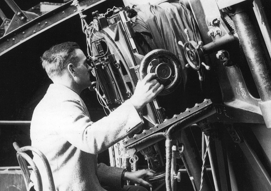 black and white photo of Edwin Hubble looking through a telescope